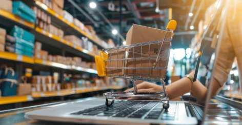 Toy shopping cart with a parcel on a laptop keyboard in a warehouse aisle