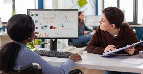 Two colleagues discussing charts on a desktop monitor